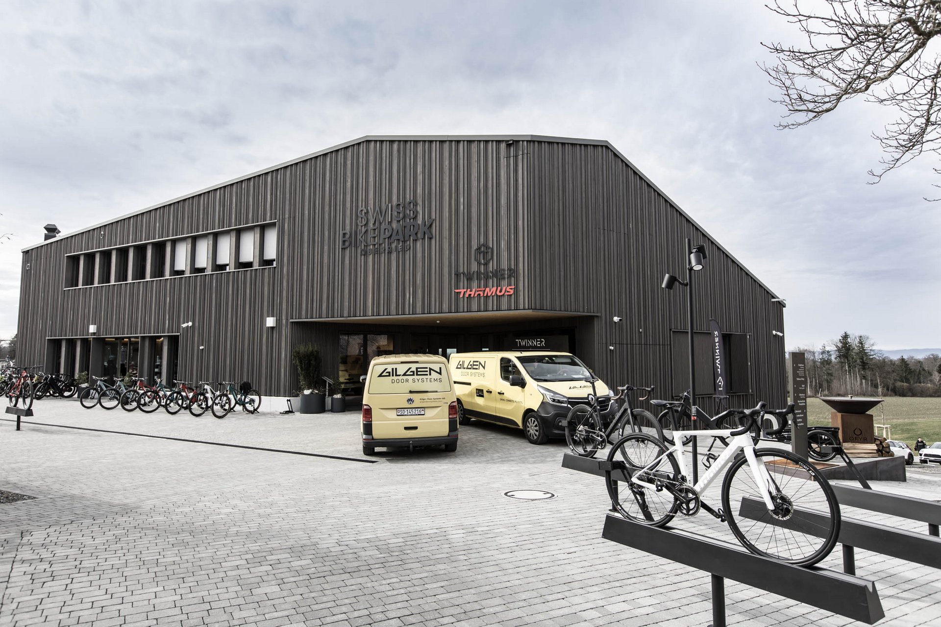Gebäude des Swiss Bike Parks in Oberried mit Kundendienstfahrzeugen von Gilgen Door Systems